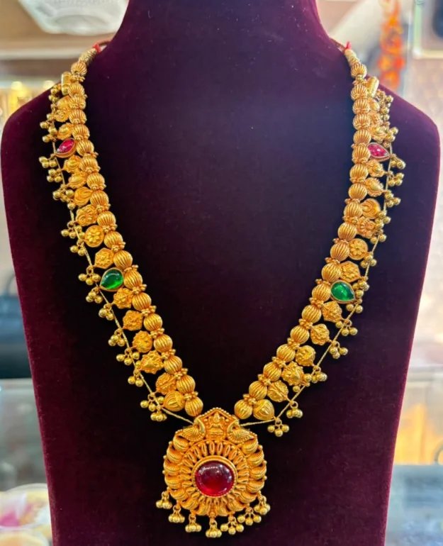 Traditional antique-finish gold necklace with a round ruby-red pendant on a velvet bust