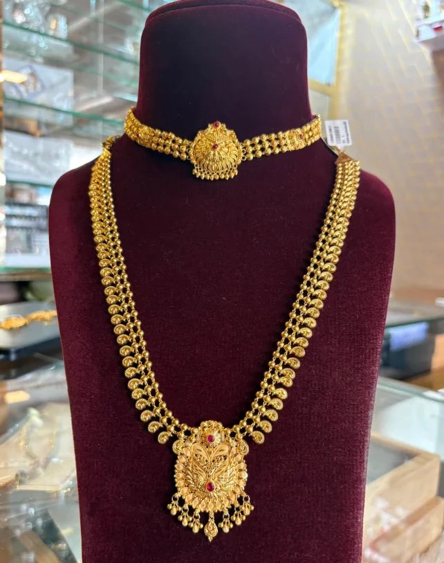 Antique-finish gold necklace with a ruby-red centre stone pendant and red and green stone accents, displayed on a maroon velvet bust at Magar Bandhu Jewellers